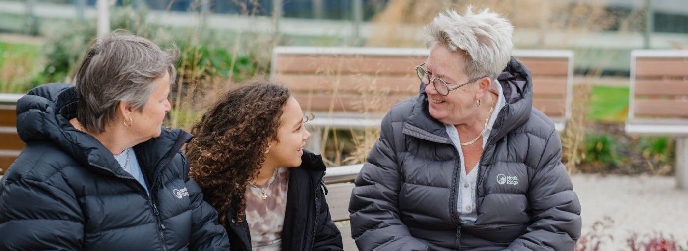 two adults sat with a child on a bench chatting